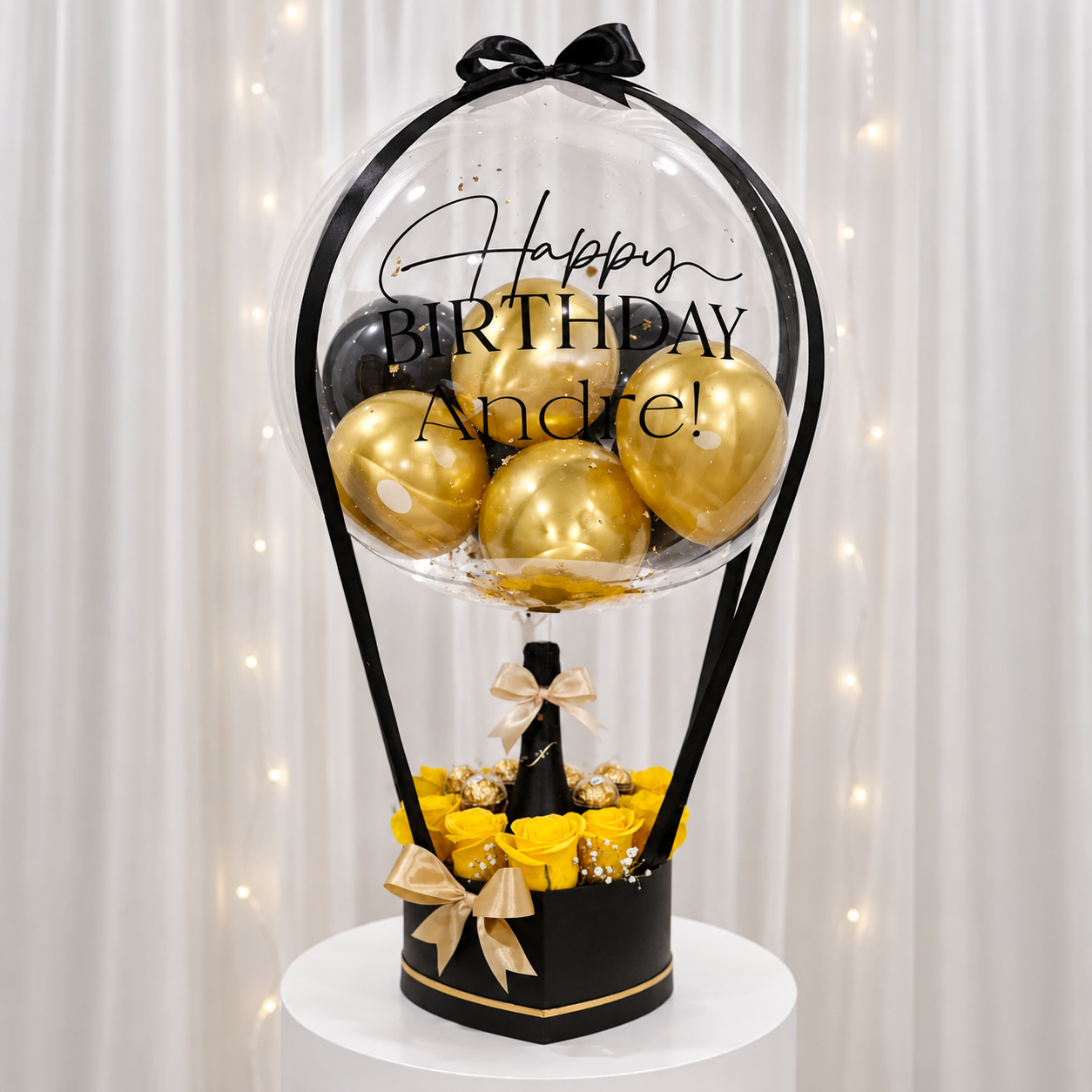 Andre’s birthday gift arrangement featuring a personalized clear balloon with black and gold balloons, yellow roses, chocolates, black and gold gift box, and satin ribbon accents.