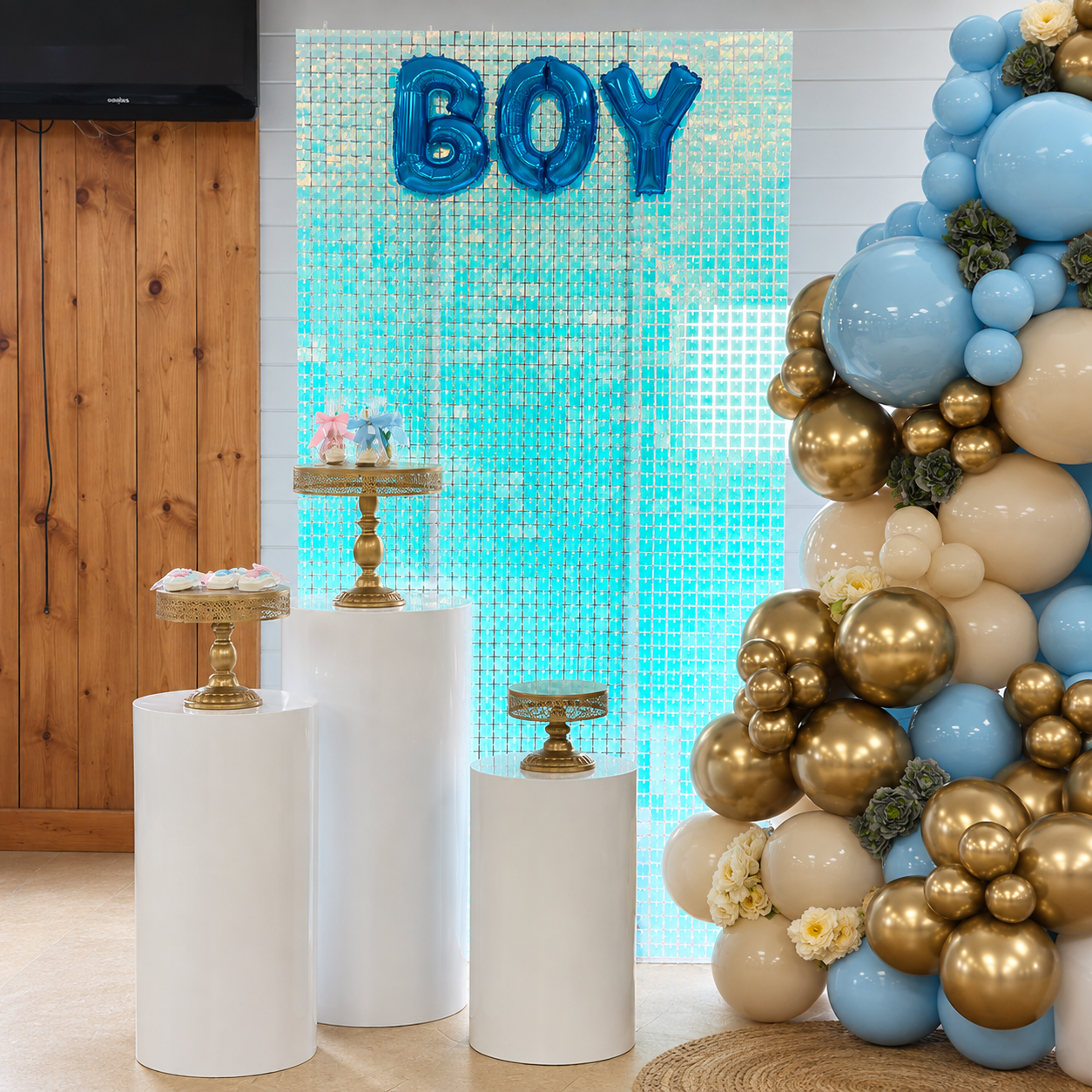 Baby gender reveal backdrop featuring blue, pink, cream, and gold balloon garlands, BOY and GIRL shimmer panels, floral accents, and a central “What Will Baby Andrew Be?” sign.