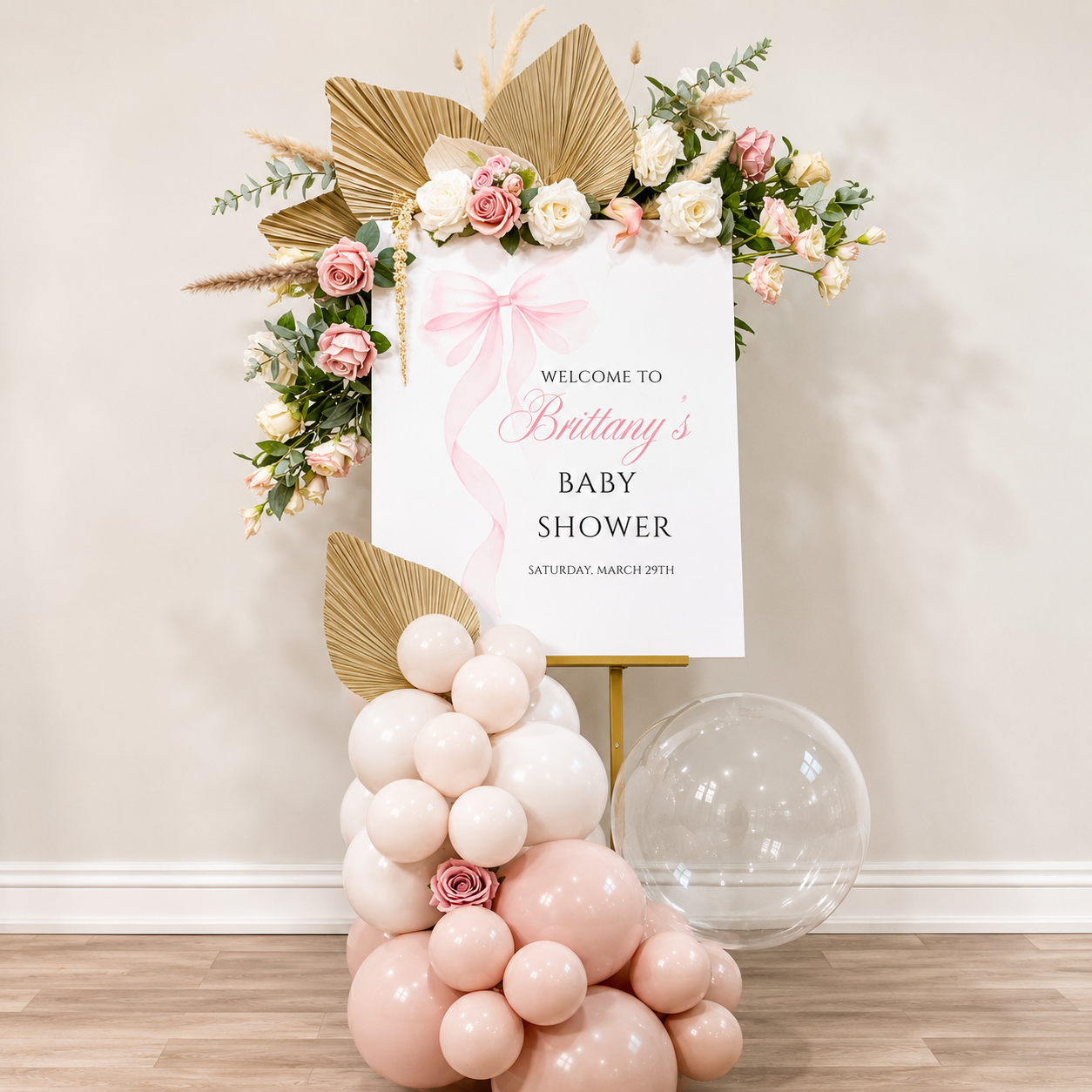 Elegant “Oh Baby” shower backdrop featuring pink, cream, and blush balloon garlands with floral accents, a white arched panel, woven rug, and vintage baby carriage filled with flowers.