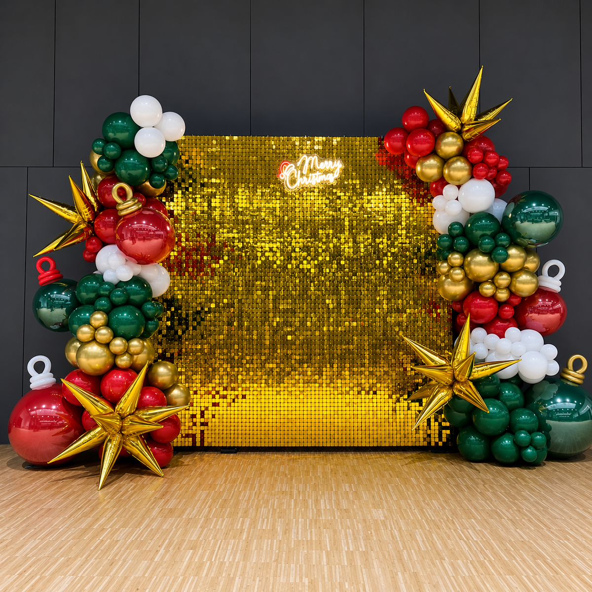 Christmas party backdrop featuring a gold shimmer wall, red, green, white, and metallic gold balloon garlands, oversized ornament balloons, gold star accents, and a glowing Merry Christmas sign.