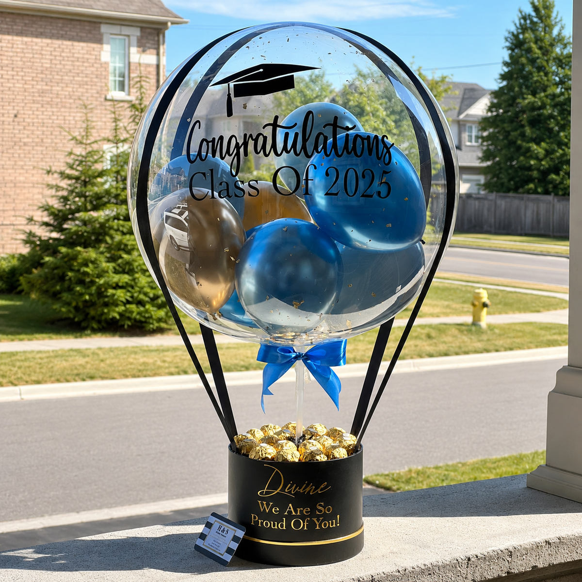 Graduation gift arrangement featuring a personalised clear balloon with blue and gold balloons, Class of 2025 message, gold-wrapped chocolates, and a black gift box.