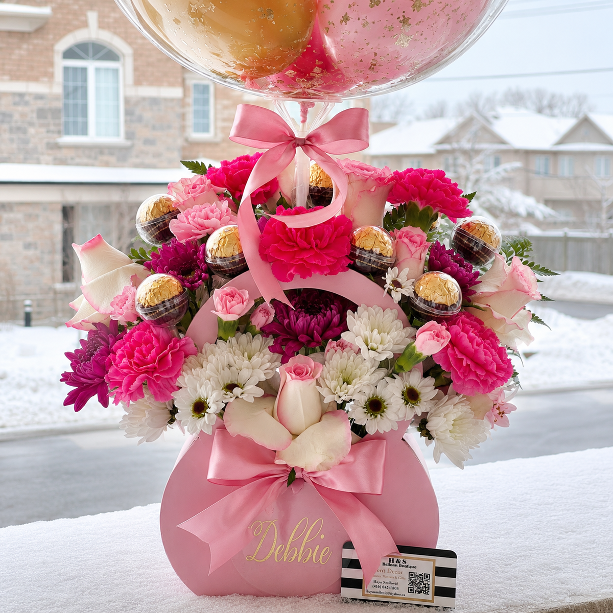 Close-up of Debbie’s 70th birthday floral arrangement featuring pink and white flowers, chocolate accents, pink satin bows, and a personalised gift box.