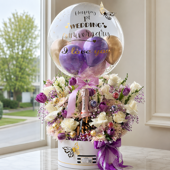 Luxury first wedding anniversary gift featuring a personalised clear bubble balloon, purple and gold balloons, flowers, butterflies, and a Prosecco bottle.