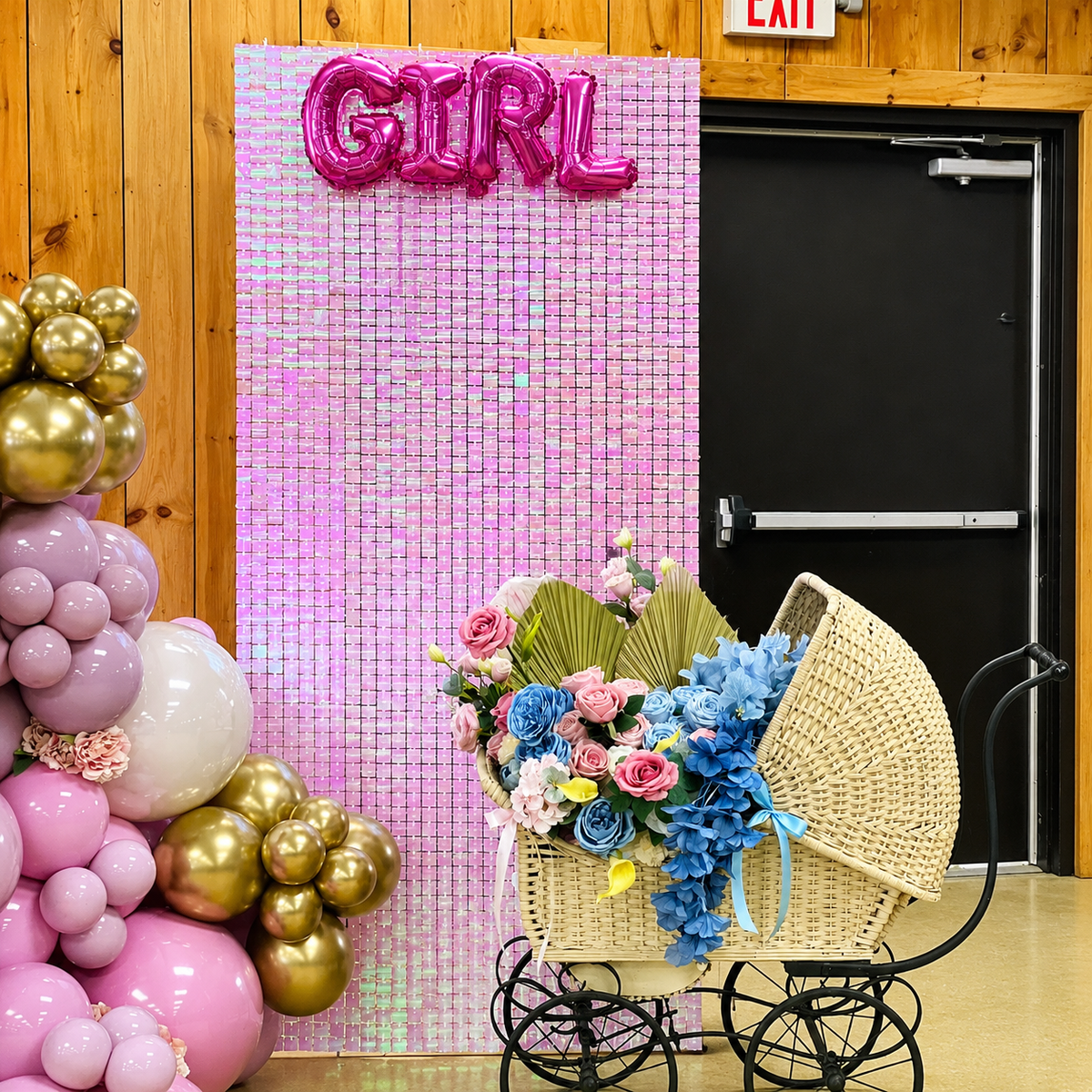 Girl gender reveal decor featuring a pink shimmer wall with GIRL balloons, pink and gold balloon accents, and a vintage baby carriage filled with pink and blue flowers