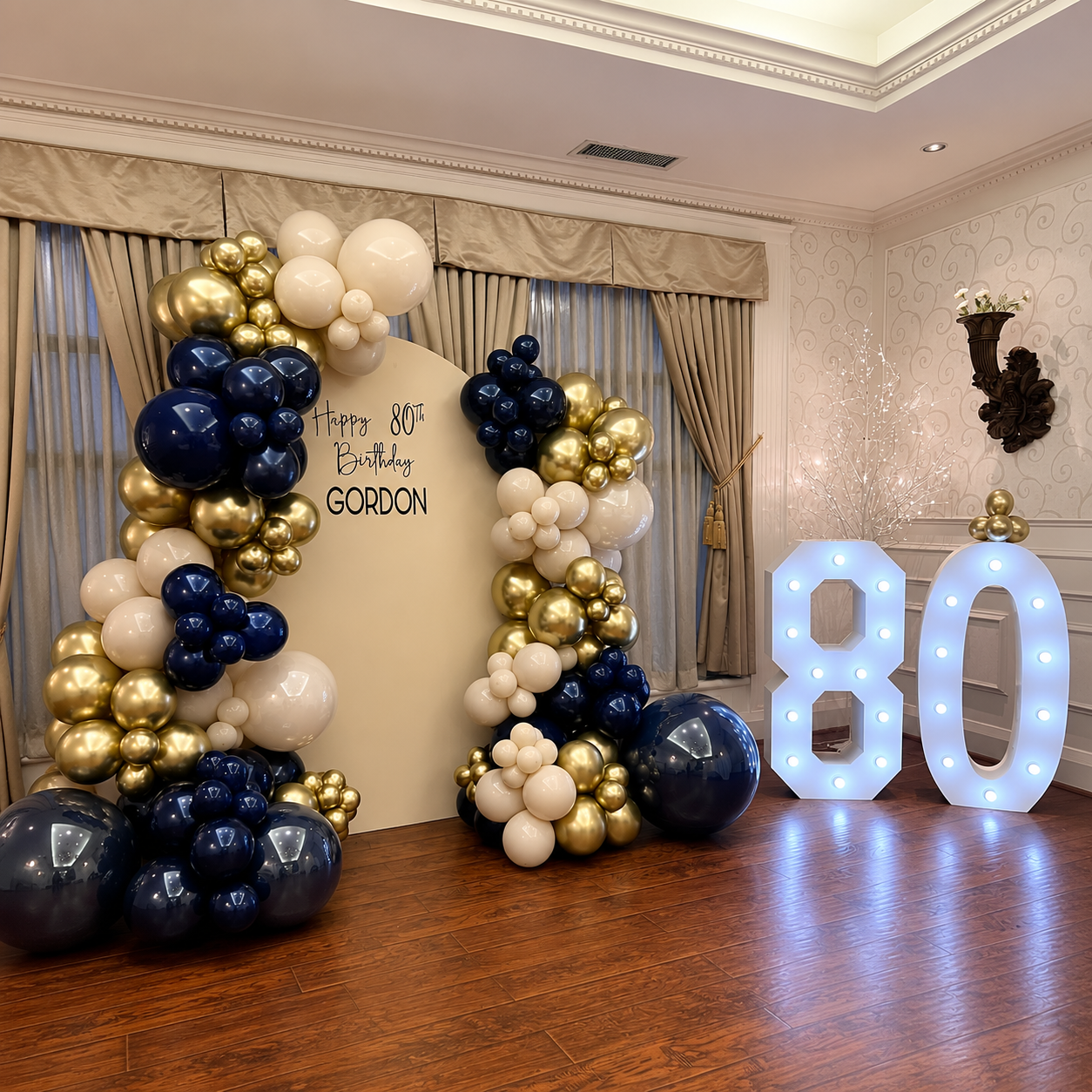 Gordon’s 80th birthday backdrop decorated with elegant navy blue, gold, and cream balloon garlands.