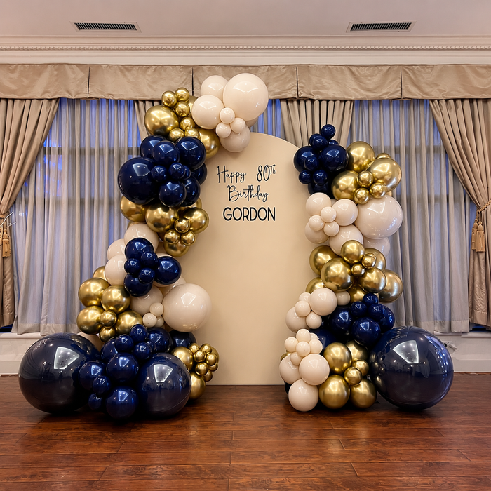Gordon’s 80th birthday backdrop decorated with elegant navy blue, gold, and cream balloon garlands.