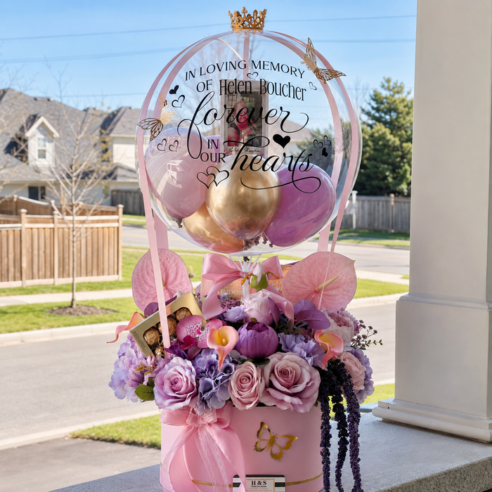 Memorial floral arrangement for Helen Boucher featuring pink and purple flowers, chocolates, butterflies, and a personalised clear balloon.