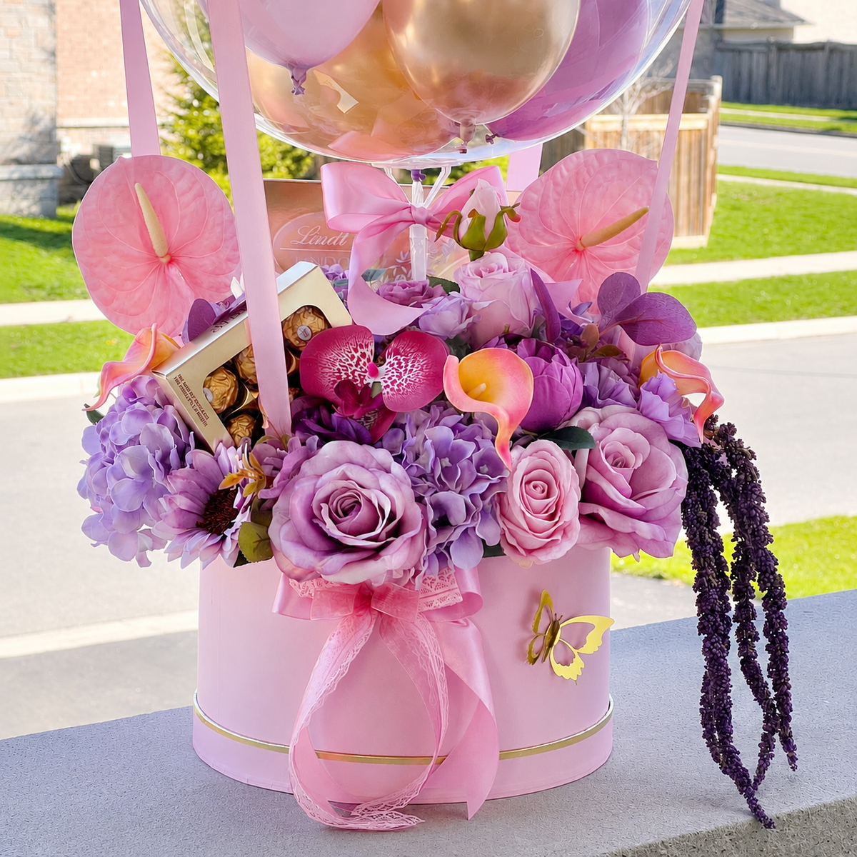 Close-up of Helen Boucher’s memorial arrangement featuring pink and purple flowers, chocolates, satin ribbons, a gold butterfly, and a clear balloon