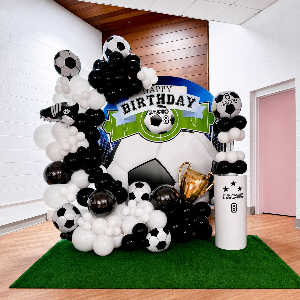 Jacob’s 8th birthday soccer-themed backdrop featuring black and white balloon garlands, soccer ball decorations, a trophy, green turf, and a personalised birthday display.