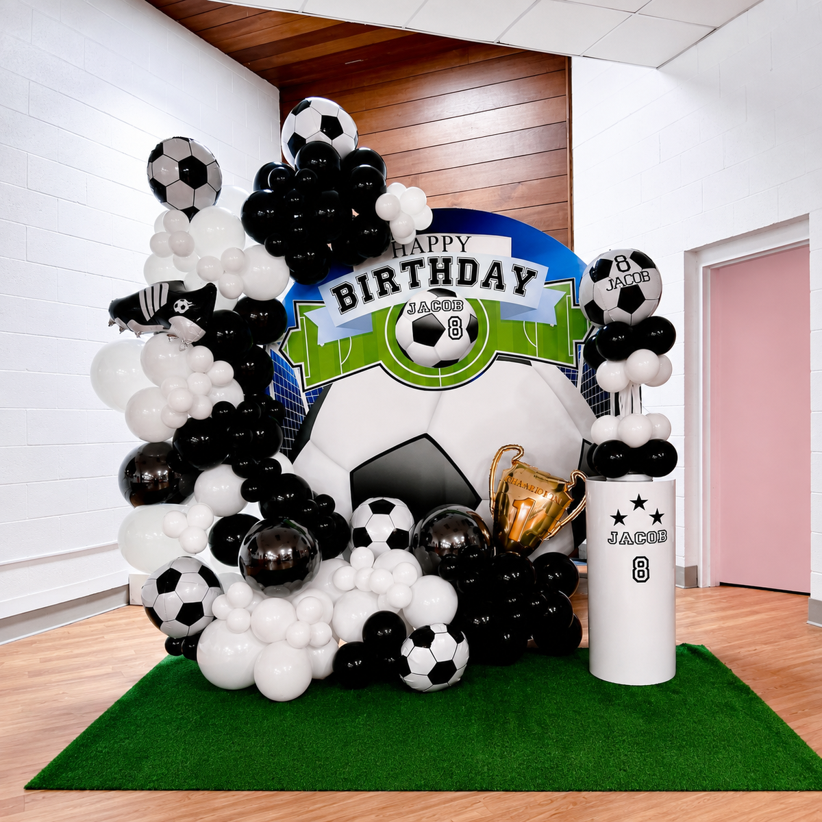 Jacob’s 8th birthday soccer-themed backdrop featuring black and white balloon garlands, soccer ball decorations, a trophy, green turf, and a personalised birthday display.