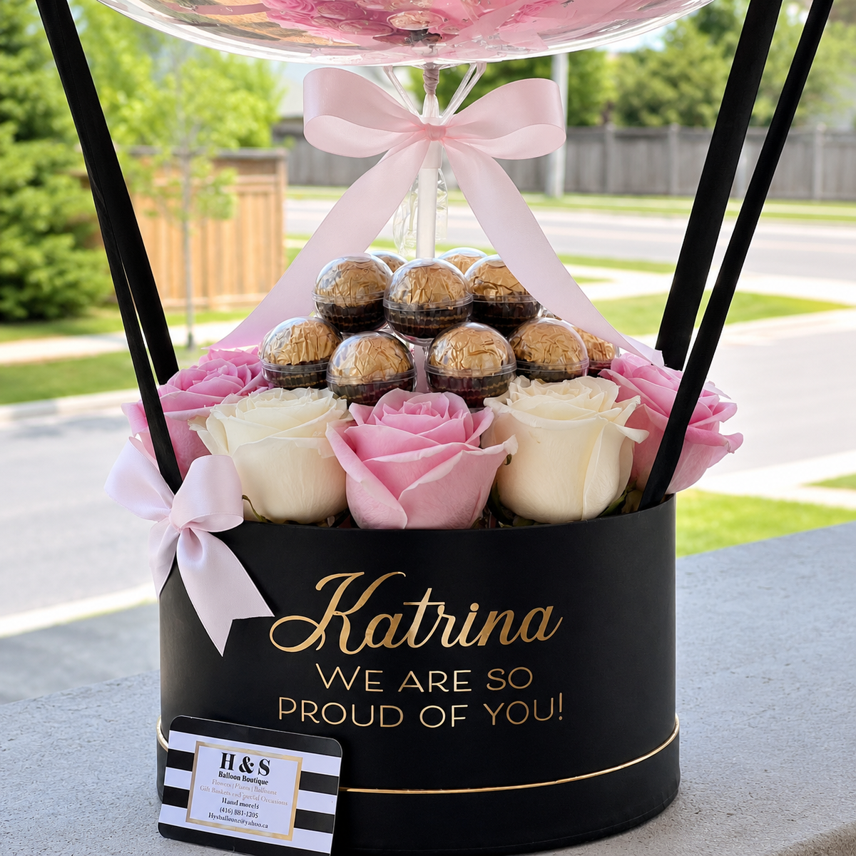 Close-up of Katrina’s graduation gift featuring pink and white roses, gold-wrapped chocolates, pale pink ribbons, and a personalised black and gold gift box.