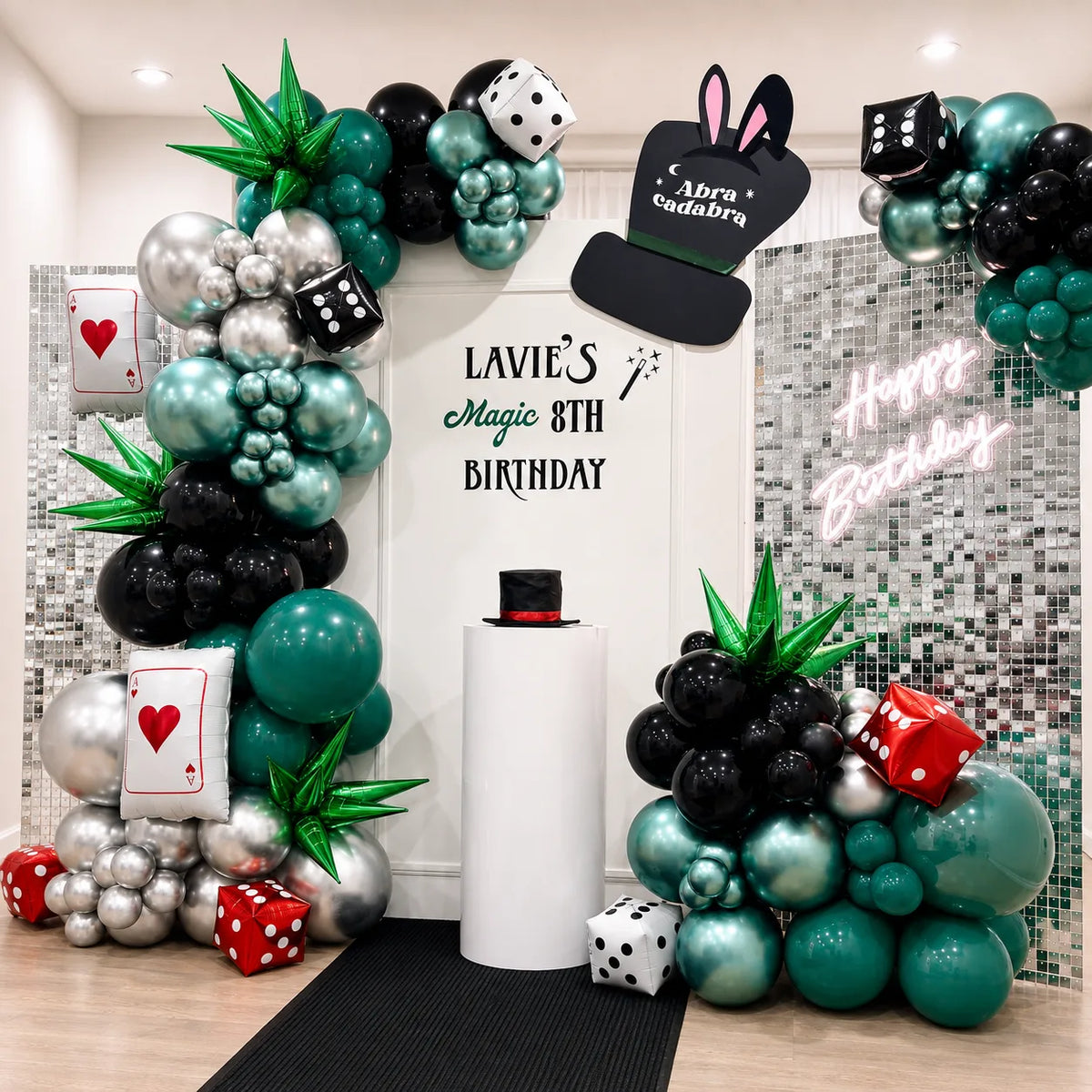Lavie’s 8th birthday magic-themed backdrop featuring green, black, and silver balloon garlands, playing cards, dice, a magician hat, and a silver shimmer wall.