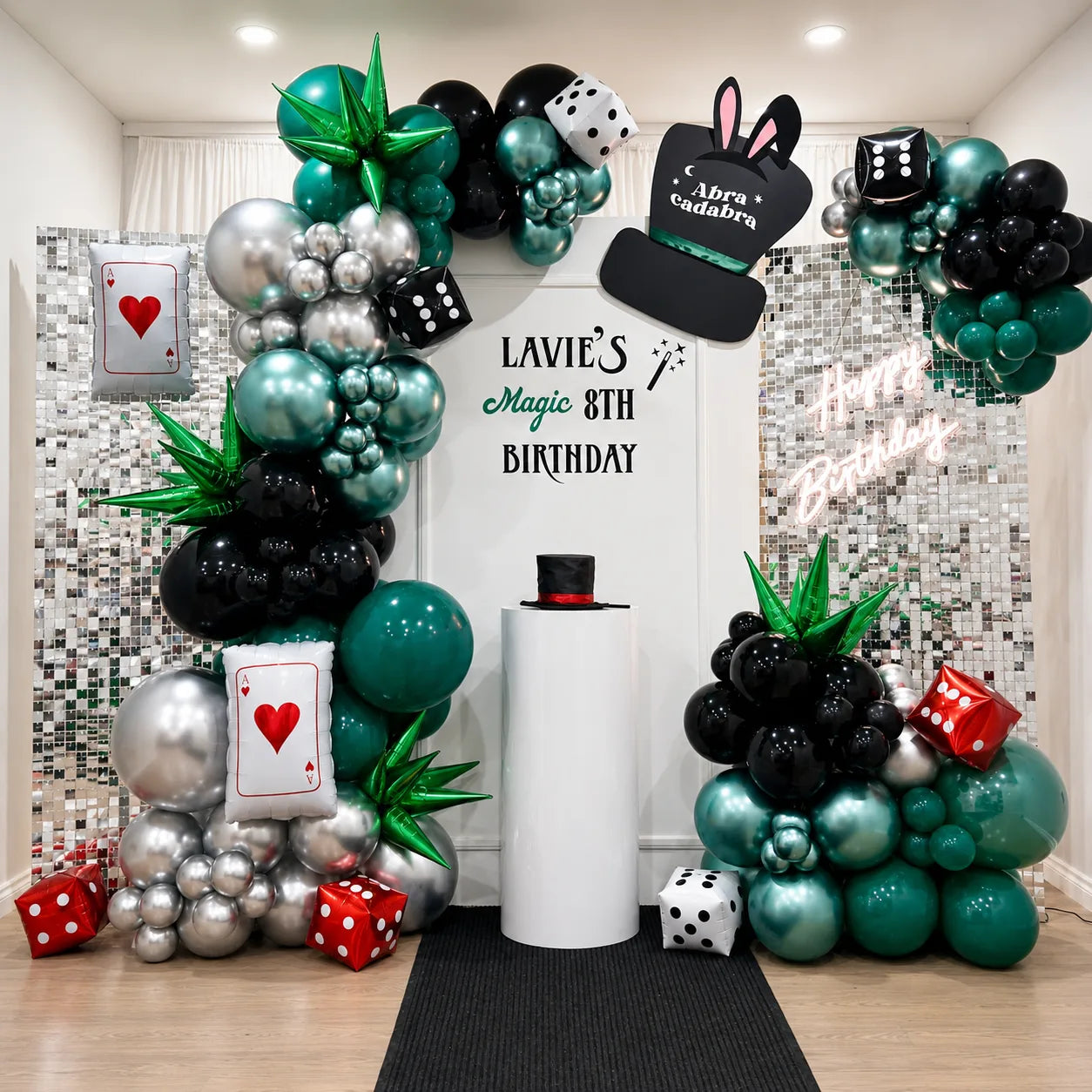 Lavie’s 8th birthday magic-themed backdrop featuring green, black, and silver balloon garlands, playing cards, dice, magician hat decor, and silver shimmer panels.