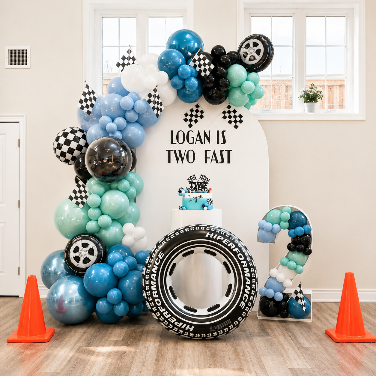 Logan’s second birthday race car backdrop featuring blue, aqua, black, and white balloon decor, checkered racing flags, tire accents, a number 2 display, and a personalised welcome sign.