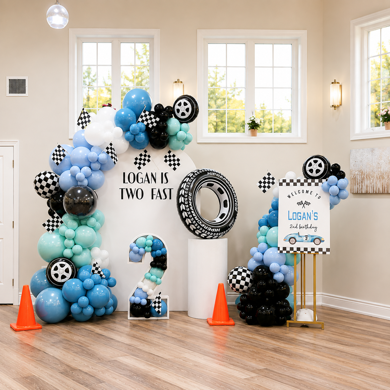 Logan’s second birthday race car backdrop featuring blue, aqua, black, and white balloon decor, checkered racing flags, tire accents, a number 2 display, and a personalised welcome sign.