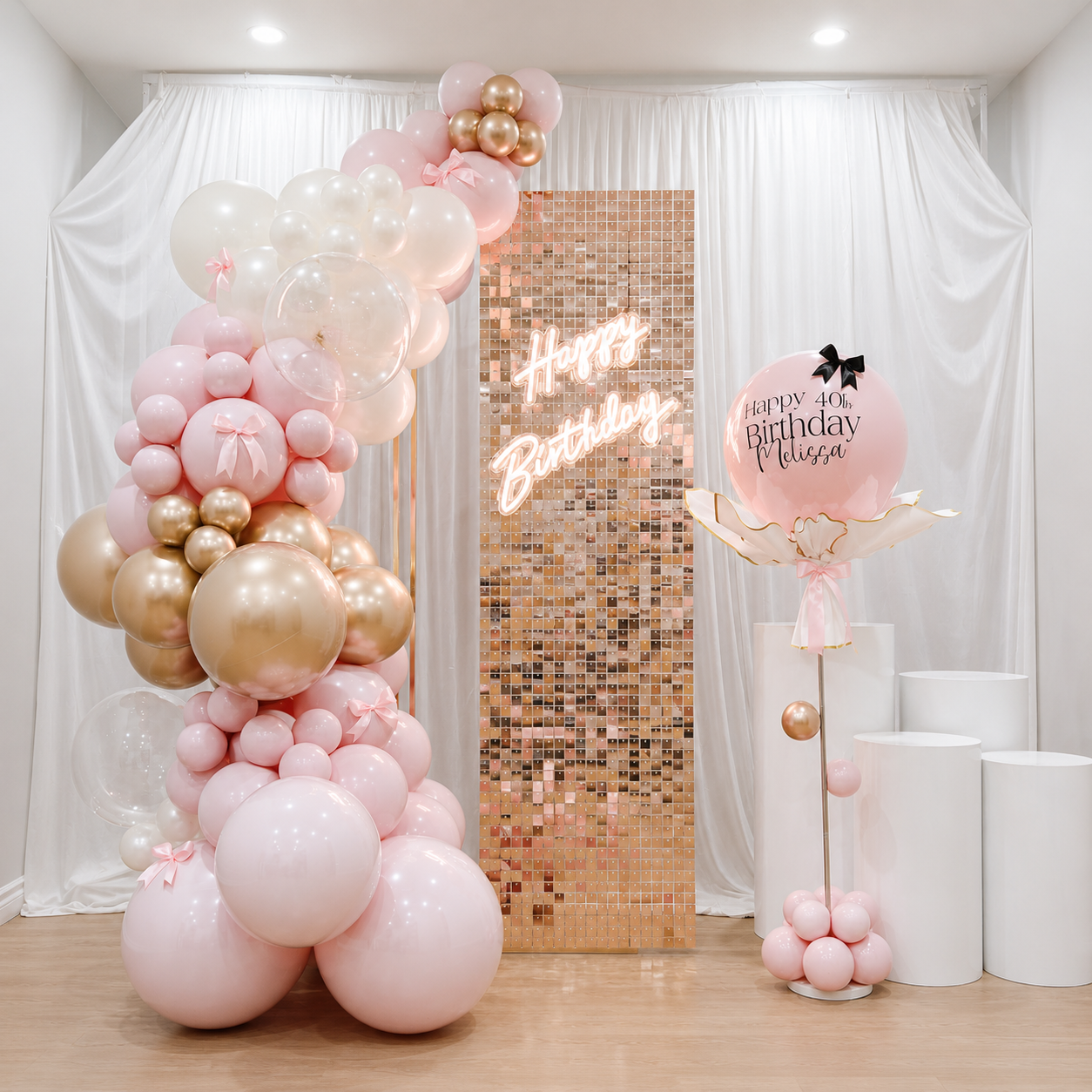Melissa’s 40th birthday backdrop featuring blush pink, white, and champagne gold balloons, a rose gold shimmer panel with Happy Birthday neon sign, personalized pink balloon, and white pedestal stands.