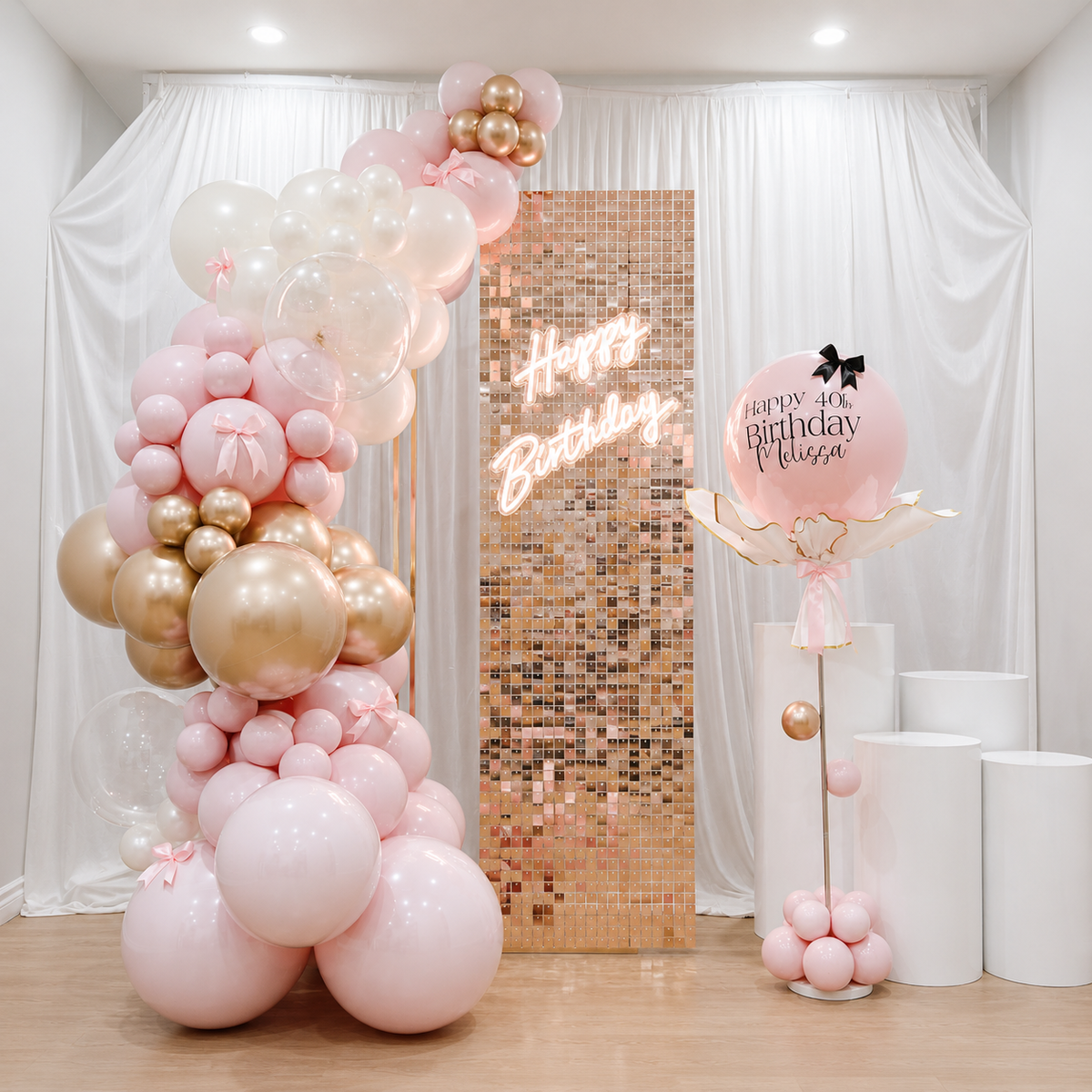 Melissa’s 40th birthday backdrop featuring blush pink, white, and champagne gold balloons, a rose gold shimmer panel with Happy Birthday neon sign, personalized pink balloon, and white pedestal stands.