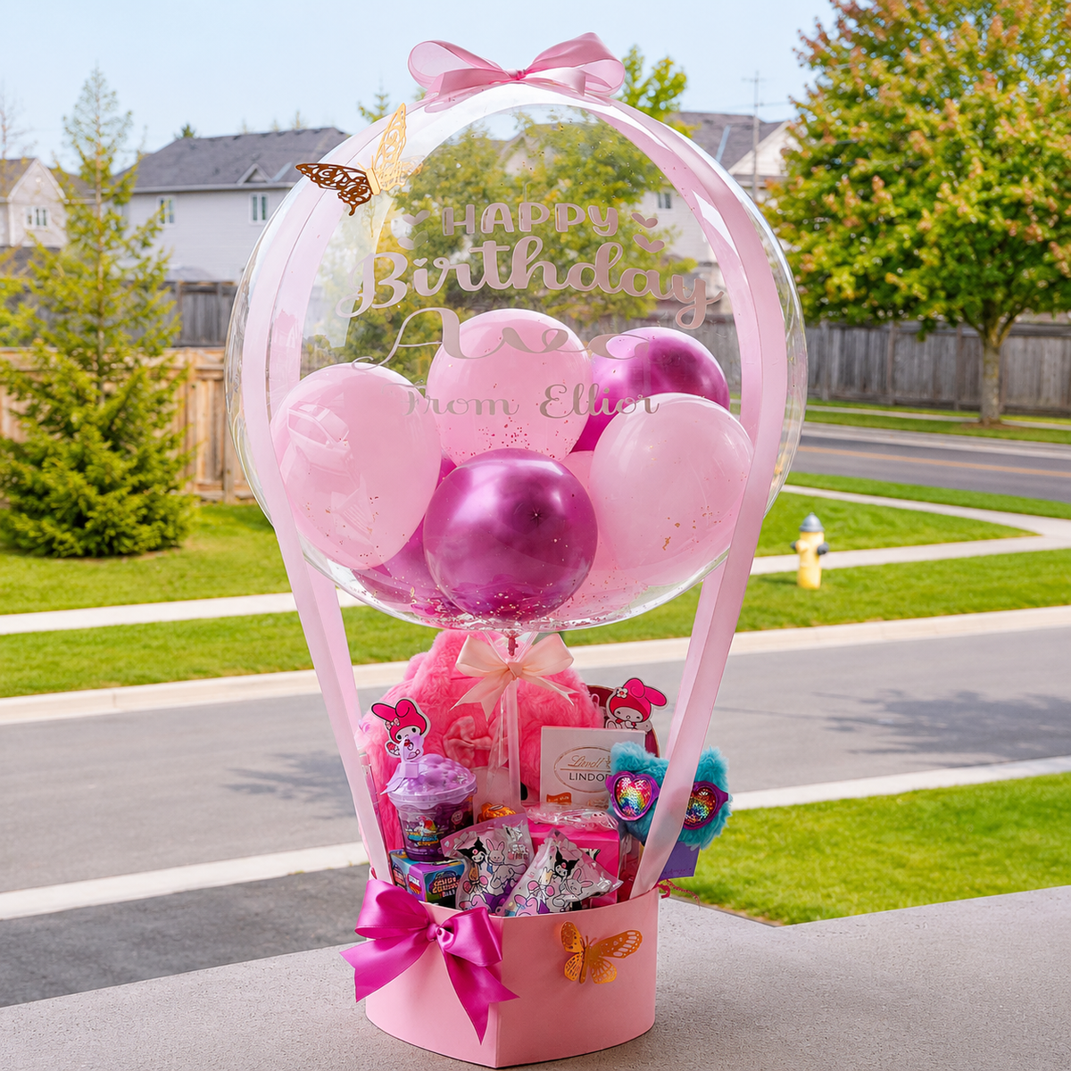 Pink My Melody themed birthday gift arrangement featuring a personalized clear balloon, pink and purple balloons, butterfly accents, sweets and gift items, and a bright pink ribbon bow.