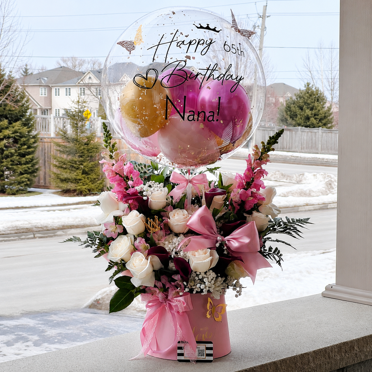 65th birthday gift for Nana featuring a personalised clear balloon, pink and gold balloons, white and pink flowers, butterflies, and elegant ribbon accents.