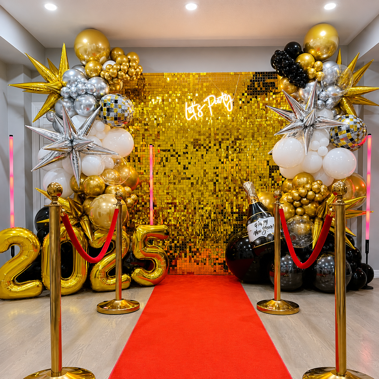 New Year’s Eve 2025 party backdrop featuring a gold shimmer wall, black, white, silver, and gold balloon garlands, metallic star balloons, disco ball accents, champagne decor, and large gold 2025 balloons.