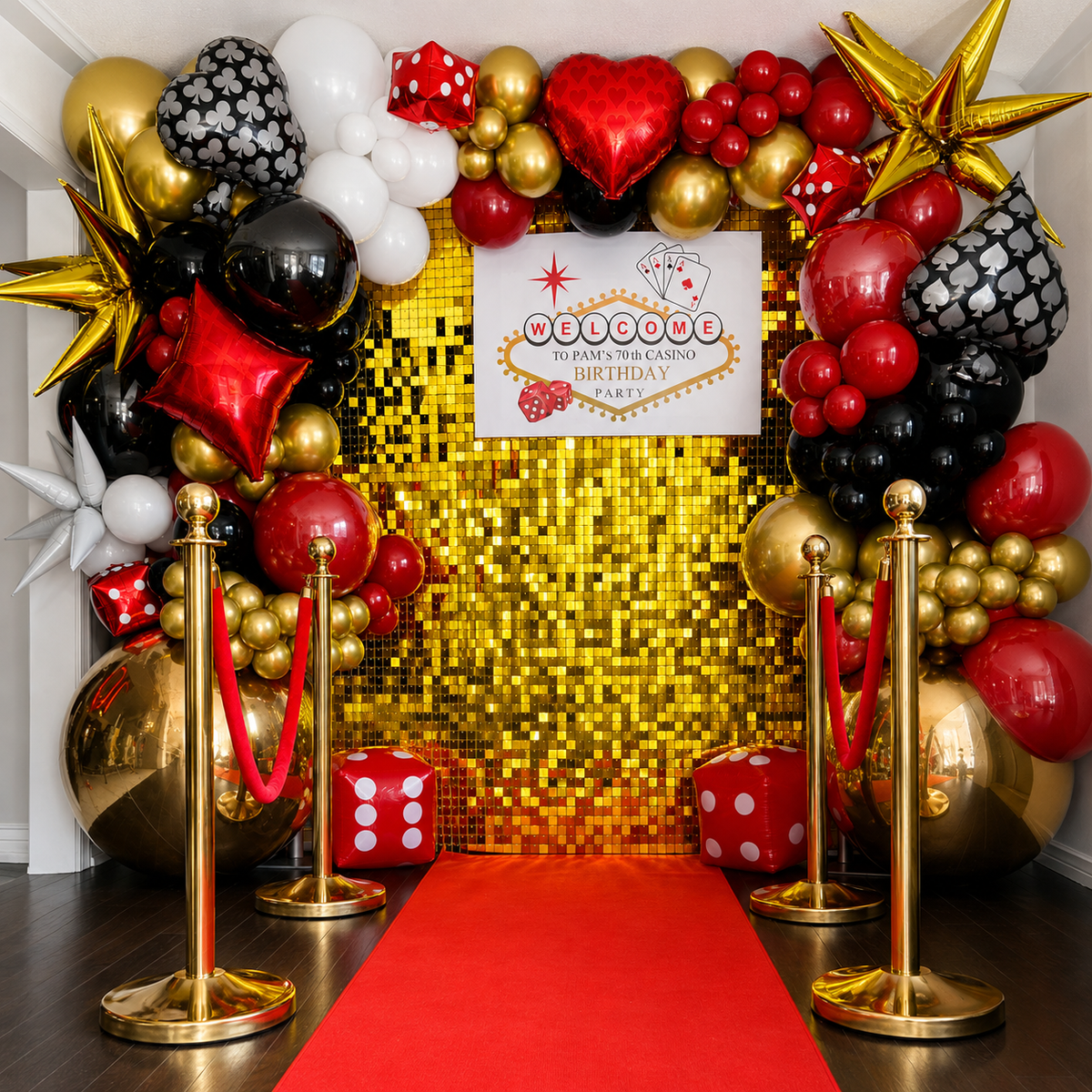 Pam’s 70th casino birthday backdrop featuring red, black, white, and gold balloons, playing card and dice decor, a gold shimmer wall, and a red carpet entrance.
