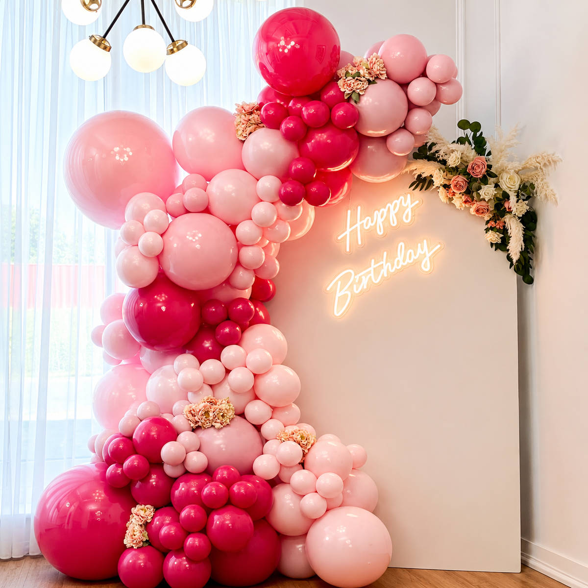 Pink birthday backdrop featuring blush and hot pink balloon garlands, floral accents, and a glowing Happy Birthday sign.