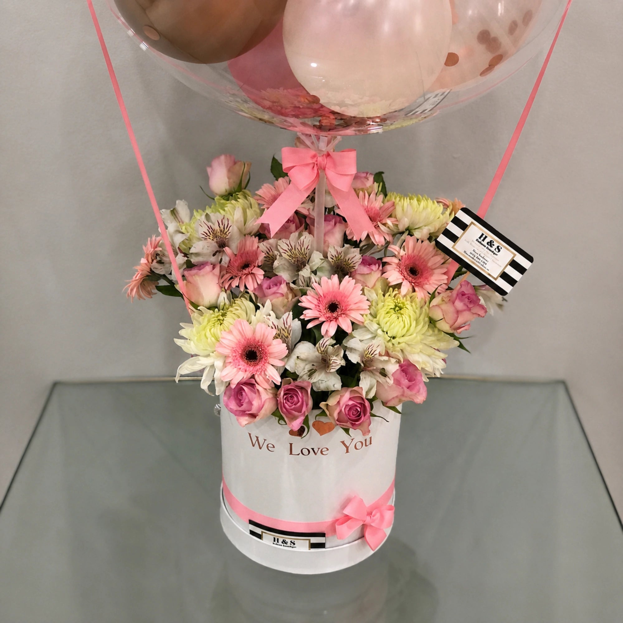 Personalized 40th birthday gift arrangement featuring a clear balloon with pink, white, and rose gold balloons, a mixed pink and white floral arrangement, heart accents, pink ribbon details, and a white “We Love You” gift box.