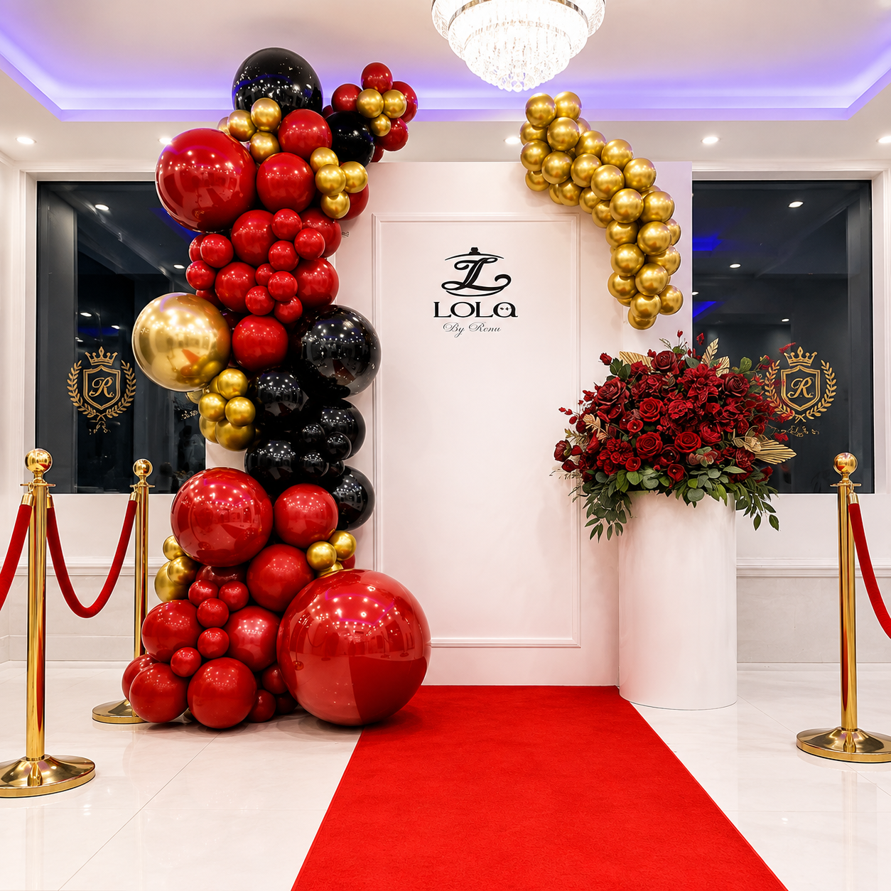 Elegant red, black, and gold event backdrop featuring heart-shaped balloons, balloon garlands, red roses, gold stanchions, clear bubble balloons, and a red carpet display.