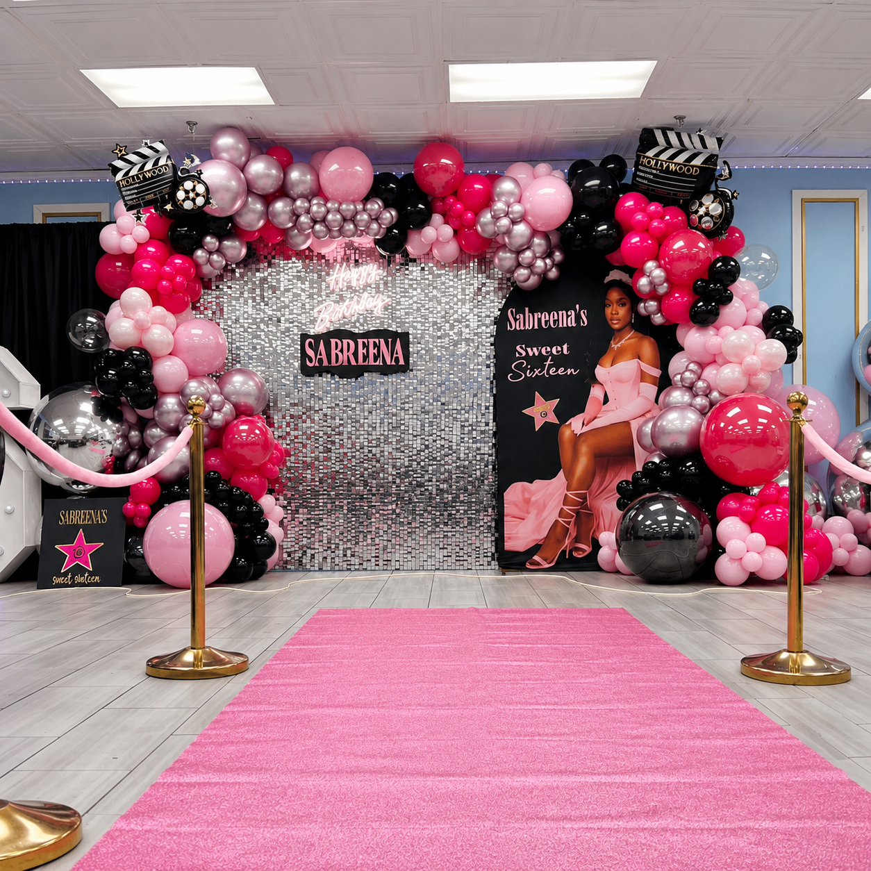 Sabreena’s Sweet Sixteen Hollywood-themed party backdrop featuring pink, black, and silver balloon garlands, a shimmer wall, movie clapboards, and a pink carpet.