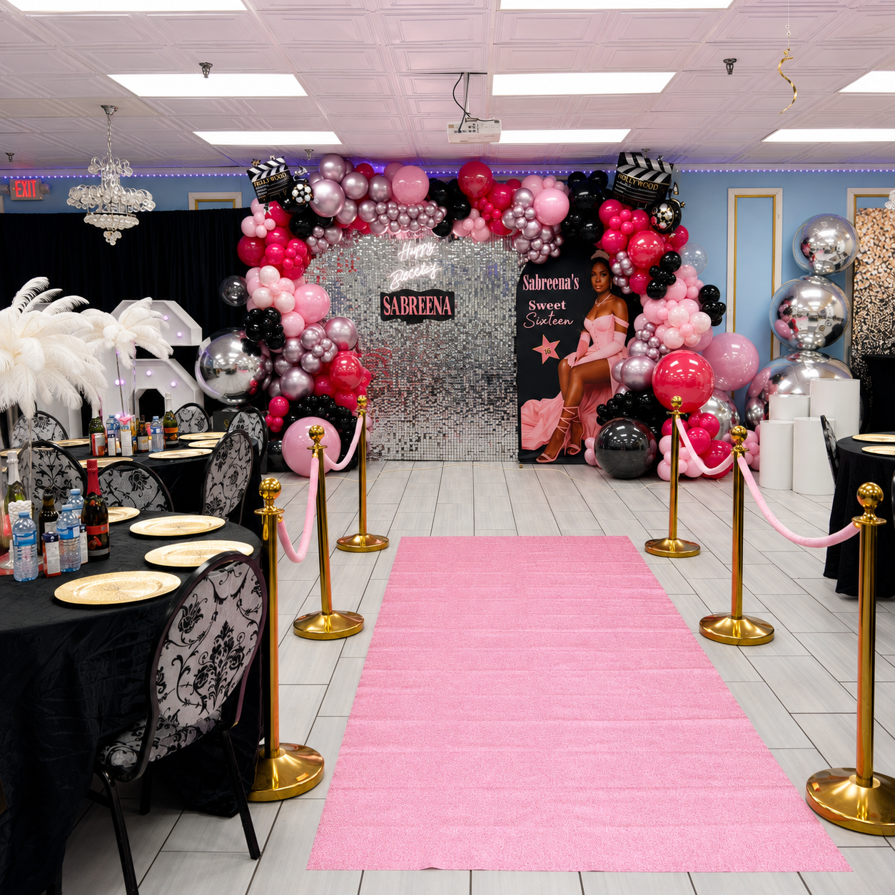 Sabreena’s Sweet Sixteen Hollywood-themed party backdrop featuring pink, black, and silver balloon garlands, a shimmer wall, movie clapboards, and a pink carpet.