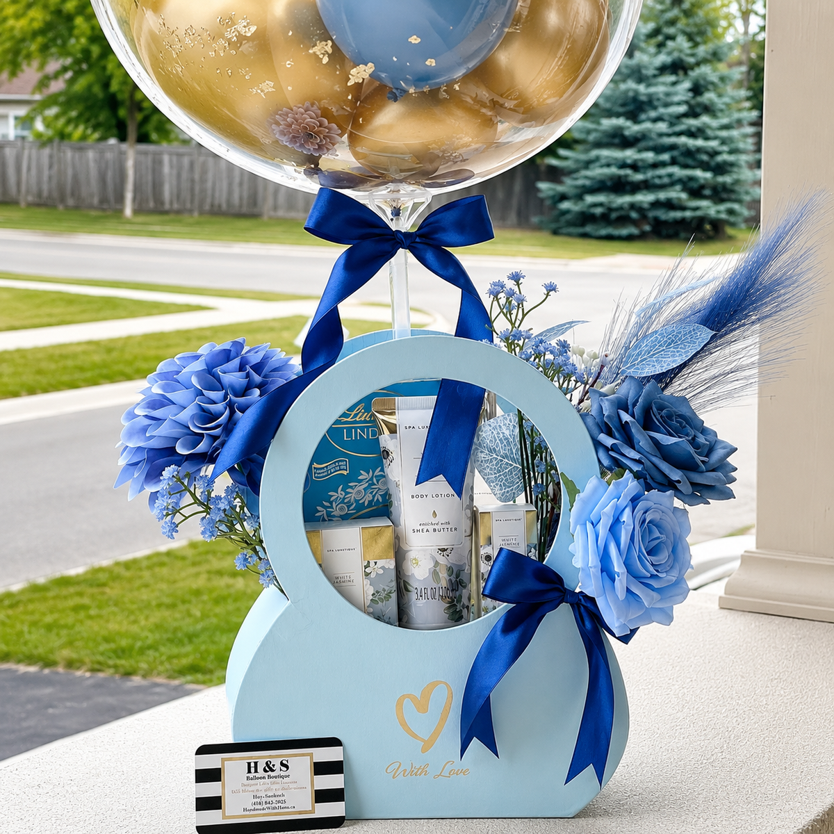 Close-up of a teacher appreciation gift arrangement featuring blue flowers, beauty products, Lindt chocolates, navy ribbons, and a personalised balloon.