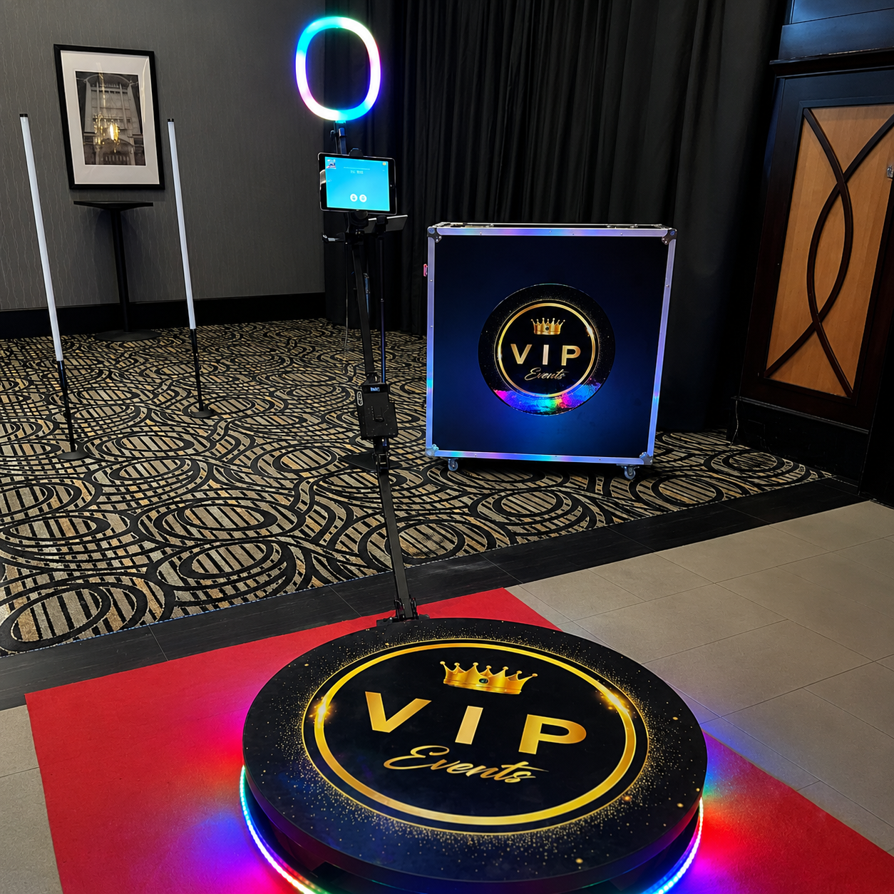VIP event setup featuring a gold shimmer wall, navy blue and metallic gold balloon garlands, a glowing “Let’s Party” sign, and a 360 photo booth platform with ring light.