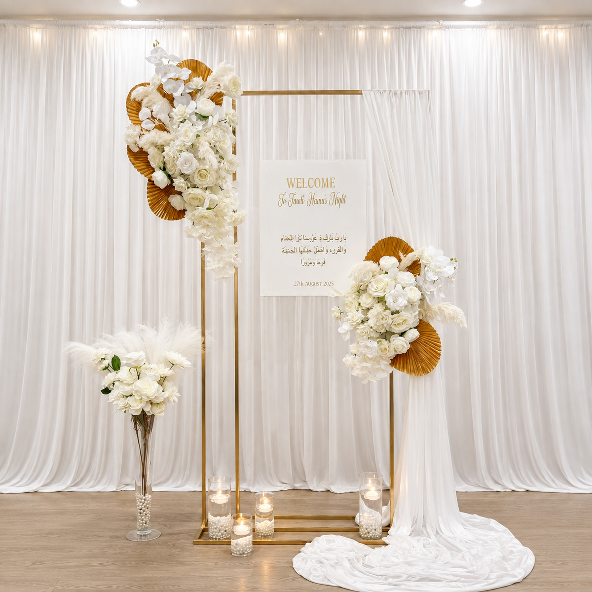 Elegant white and gold event backdrop featuring white floral arrangements, a gold frame, draped fabric, candles, and a personalised welcome sign.