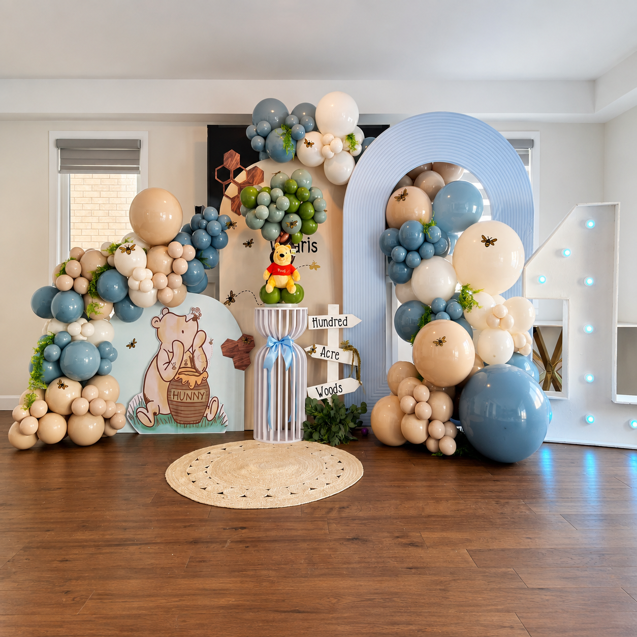 Waaris’ first birthday backdrop featuring a Winnie the Pooh theme, blue, beige, and white balloon garlands, honeybee decorations, and a large illuminated number one.